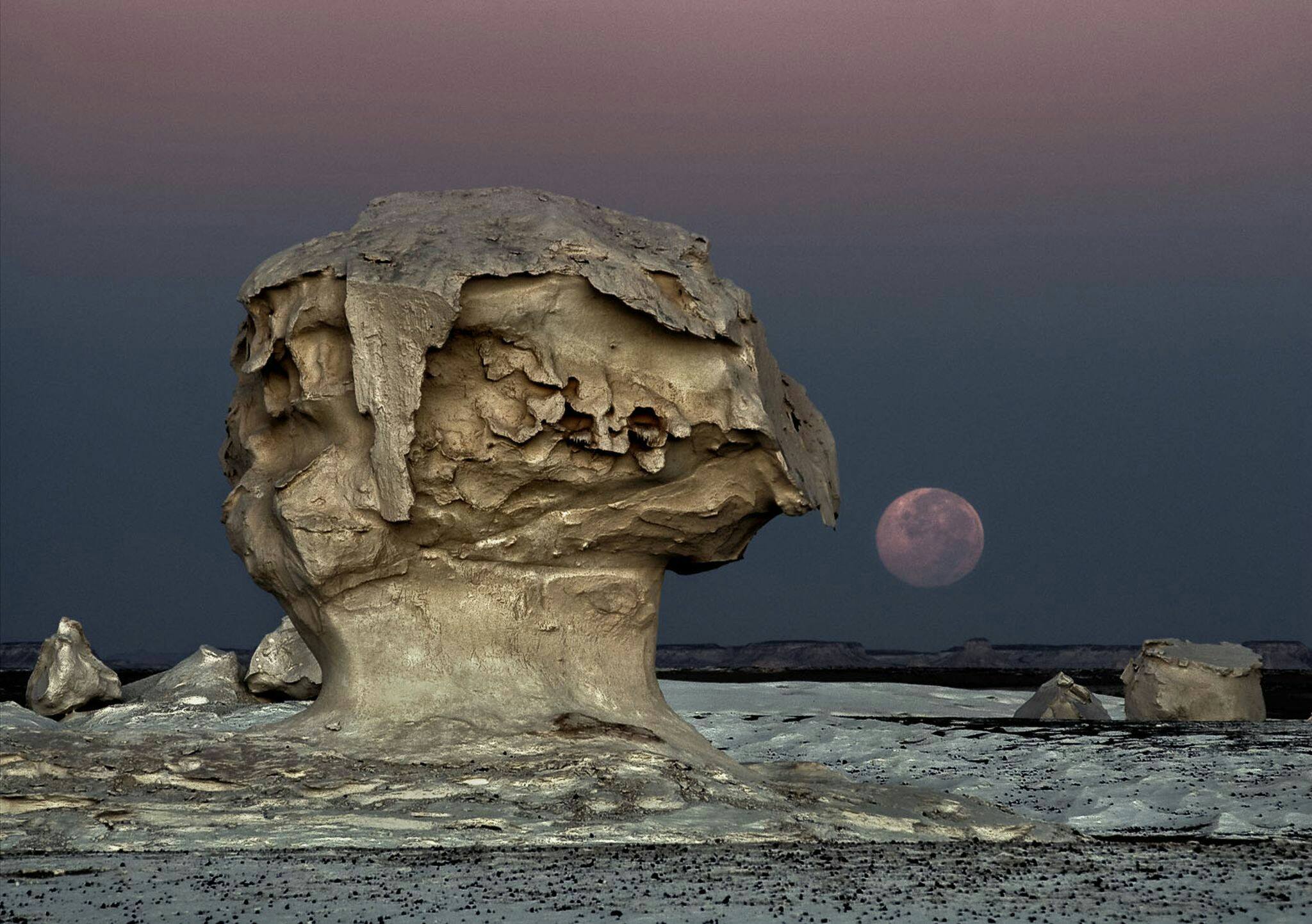 La Luna sorge nel Deserto Bianco, Egitto. La vedete quella struttura a fungo in primo piano? È un classico esempio di fungo di roccia, una forma originata dall'azione eolica in climi aridi: il vento a bassa quota trasporta infatti un maggior quantitativo di detriti sabbiosi più ci si abbassa di quota; questi detriti generano abrasione differenziale sulla roccia dando origine alla tipica forma a fungo. Strutture simili sono i pilastri di terra e le colonne di ghiaccio, ma la loro genesi è differente: i pilastri di terra si formano quando una roccia resistente all'acqua protegge la colonna di terra sottostante dalle intemperie, e le colonne di ghiaccio quando una roccia presente in un ghiacciaio protegge la colonna di ghiaccio sottostante dallo scioglimento dovuto all'irradiazione solare. Fonte foto: National Geographic